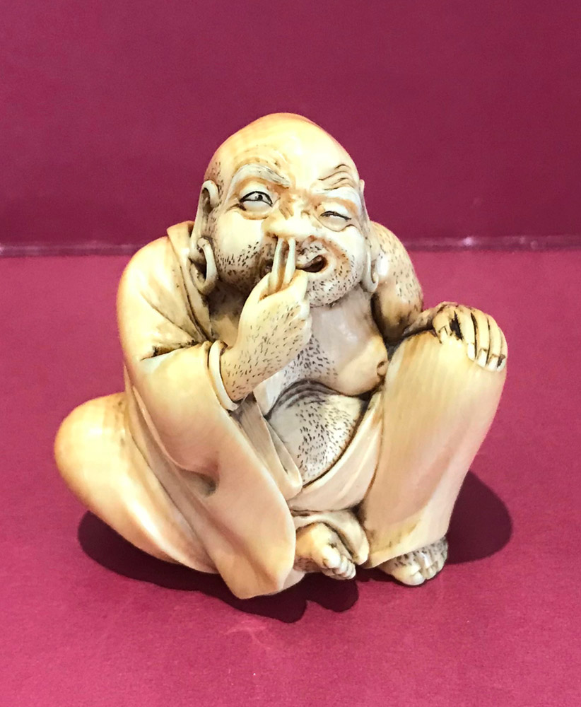 Ivory netsuke of hotei tweezing his nose hair