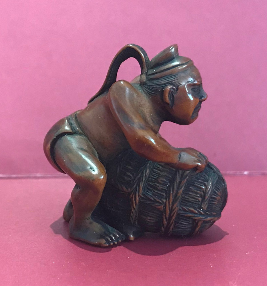 Boxwood netsuke of a man wearing a court hat lifting a rice bale